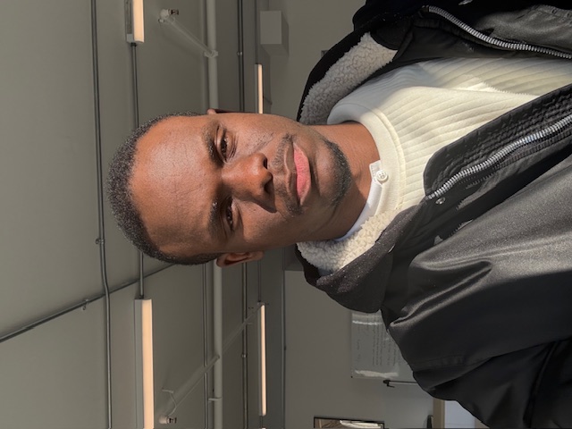 Stéphane Agoume smiling in a red plaid shirt and tortoise shell glasses